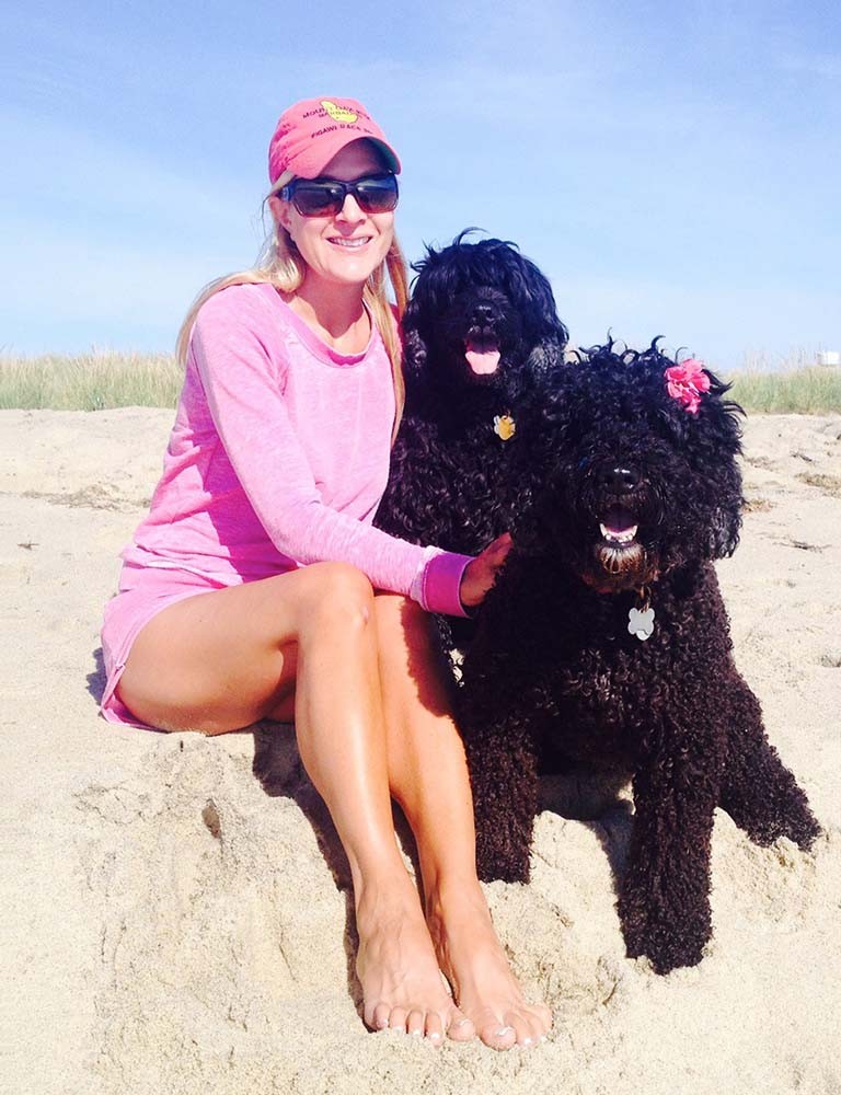 Marci sentada à praia com seus dois cachorros.